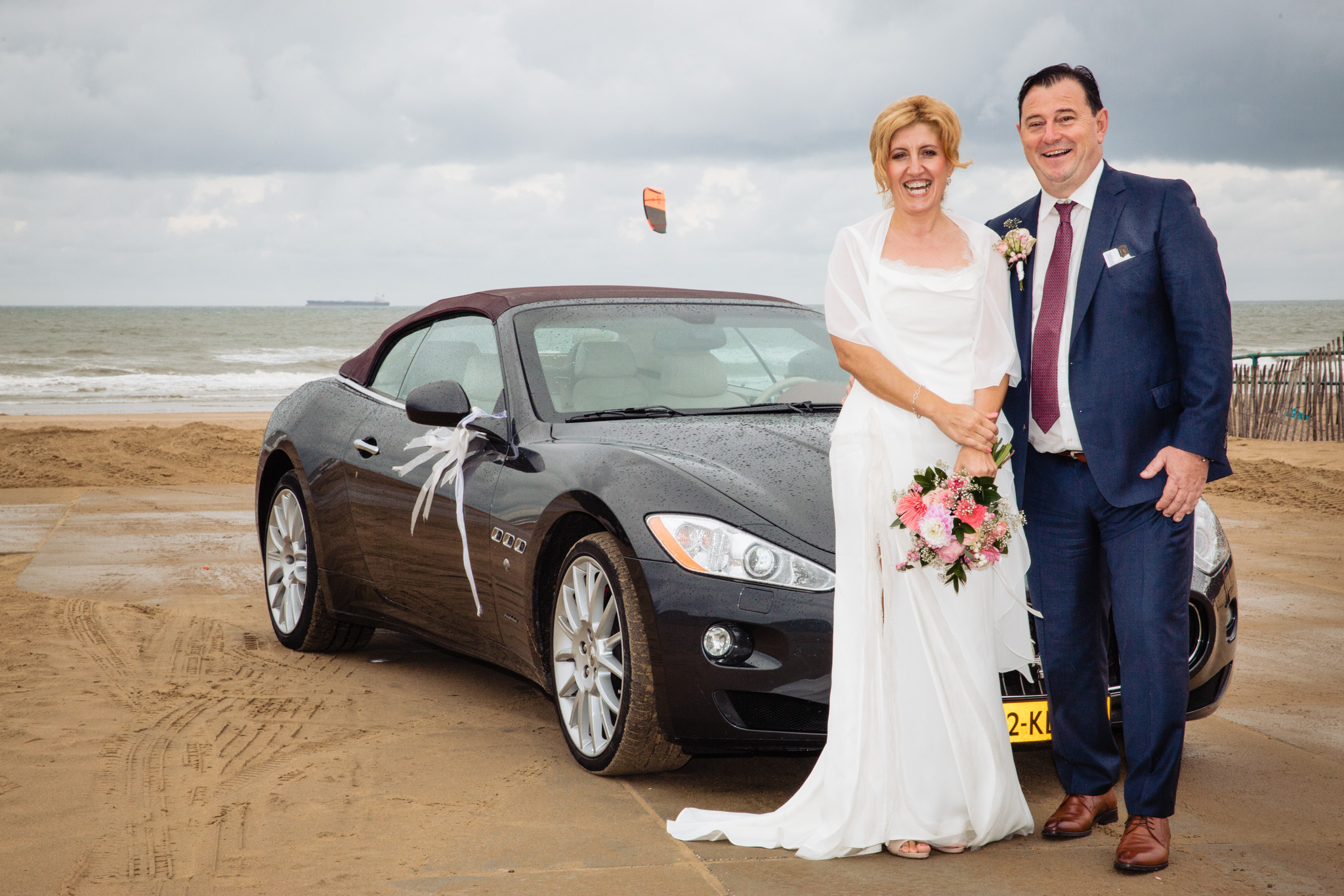 bruidspaar met auto op het strand voor de fotoreportage